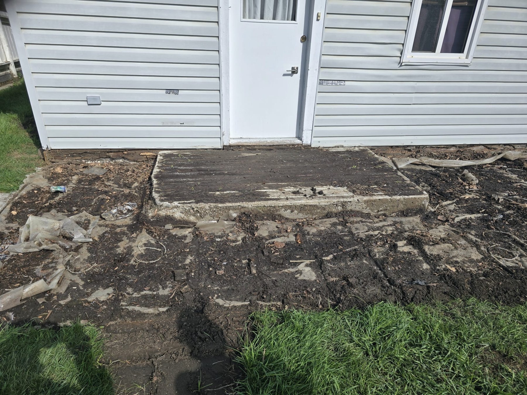 White house back door with a concrete pad and muddy ground before deck construction