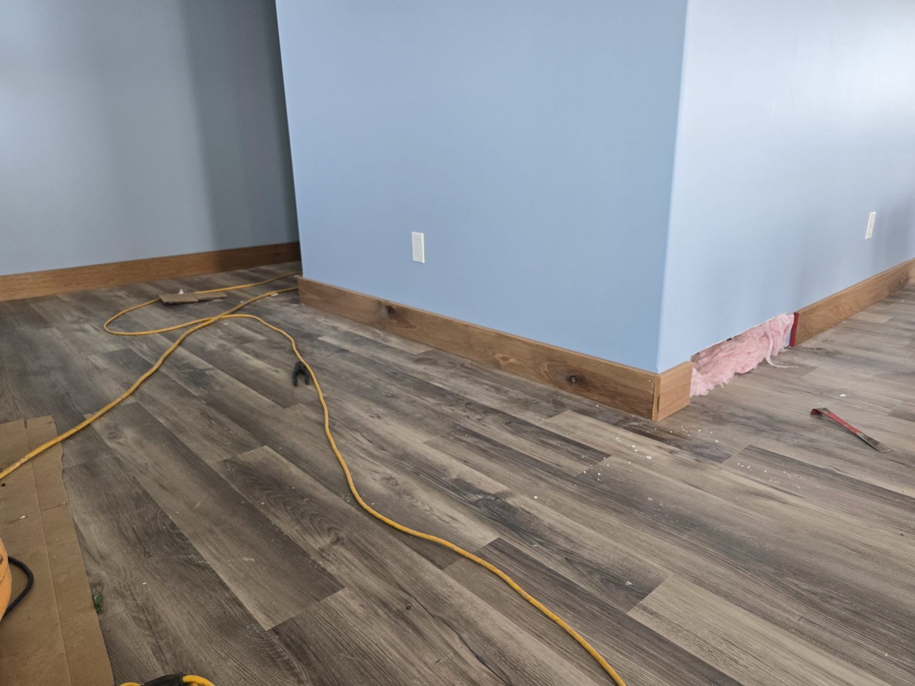 Installed wood baseboards and flooring around a blue interior wall